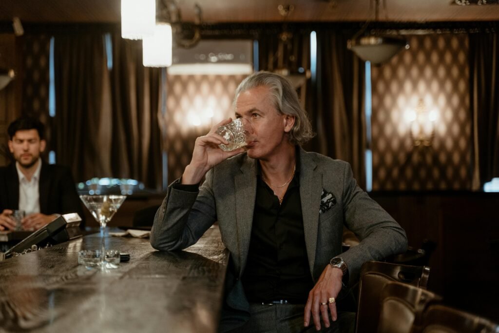 A man in a gray suit enjoys a drink at an elegant bar, exuding sophistication and style.